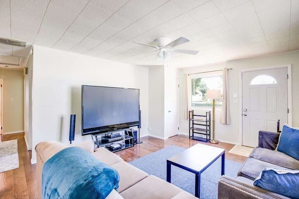 Een woonkamer met een flatscreen televisie, een plafondventilator, een bank en een salontafel.