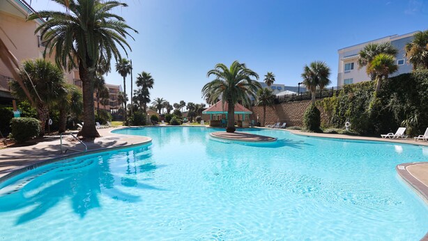 Ein Swimmingpool mit Palmen, Liegestühlen und einem Gebäude im Hintergrund.
