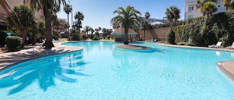 A swimming pool with palm trees, lounge chairs, and a building in the background.