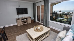 Ein Wohnzimmer mit Fernseher, einer Holzunterhaltungseinheit und Blick auf den Strand.