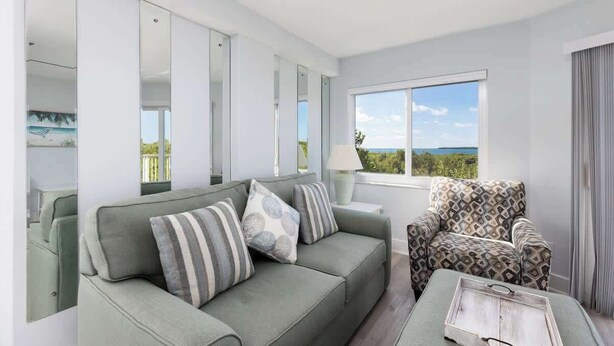 A modern living room with a sofa, patterned armchair, and a view of the outdoors. - Spacious End Suite with Atlantic Views (Tavernier)