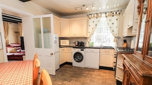 A compact kitchen with a washing machine, microwave, and stove. There is a dining area with a table and chairs. - Scotch Hall Cottage (Llangollen)