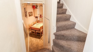 A staircase leading to a dining area with a table and chairs, a fire extinguisher, and a framed picture on the wall. - Scotch Hall Cottage (Llangollen)