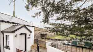 A white building with a black door, a small porch, and a stone bridge in the background. - Scotch Hall Cottage (Llangollen)