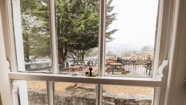 A view through a window with a stone pathway, picnic tables, and a chain-link fence. - Scotch Hall Cottage (Llangollen)