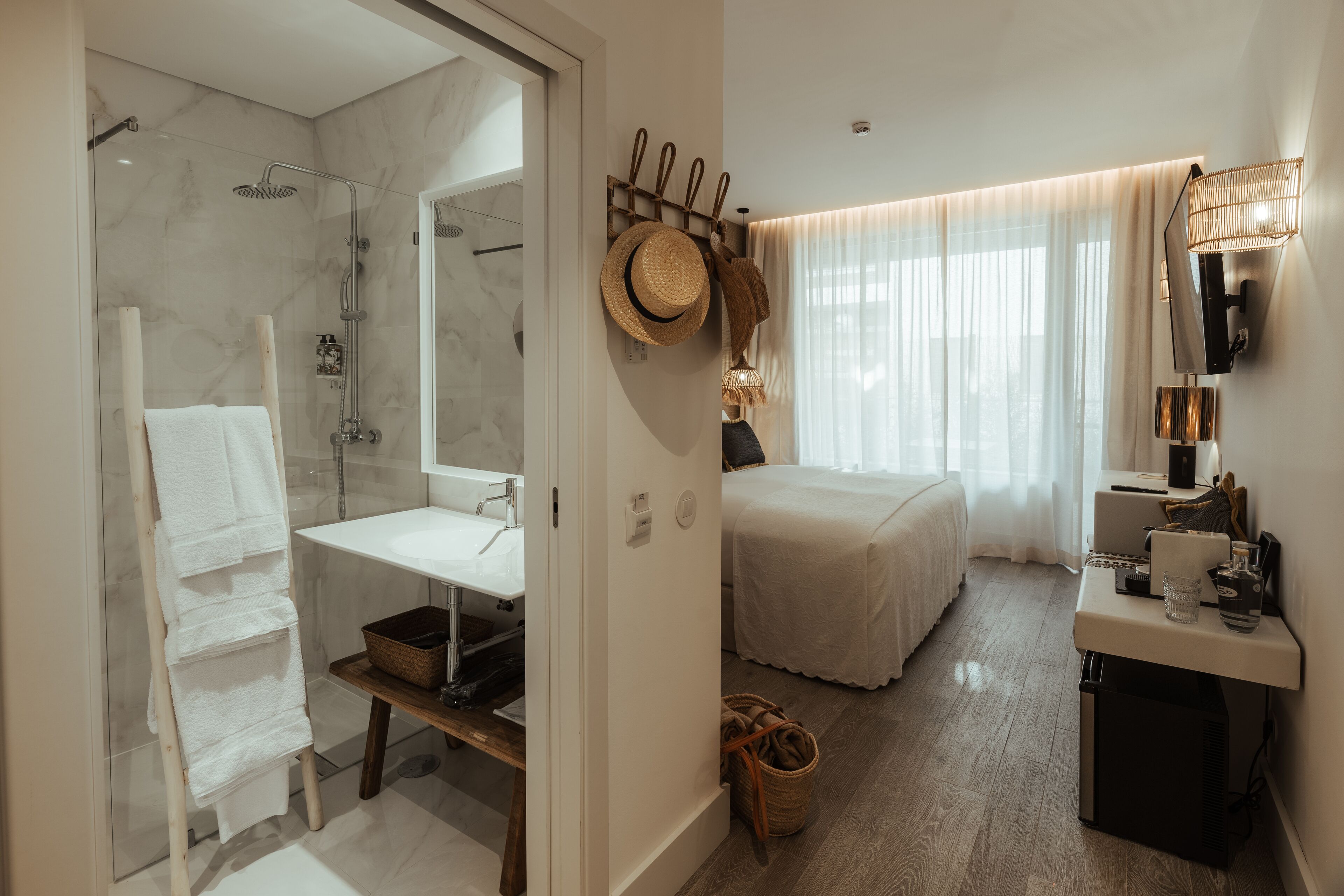 Een moderne hotelkamer met een douche, wastafel, bed en nachtkastje met lamp.