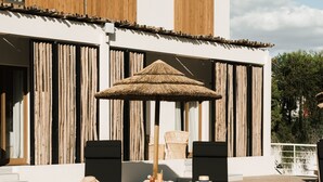 A poolside area with two lounge chairs, a small wooden table, and a thatched umbrella.