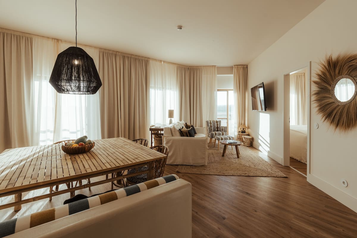 Ein modernes Wohnzimmer mit Esstisch aus Holz, einer Couch, einem an der Wand montierten Fernseher und einem großen Spiegel.