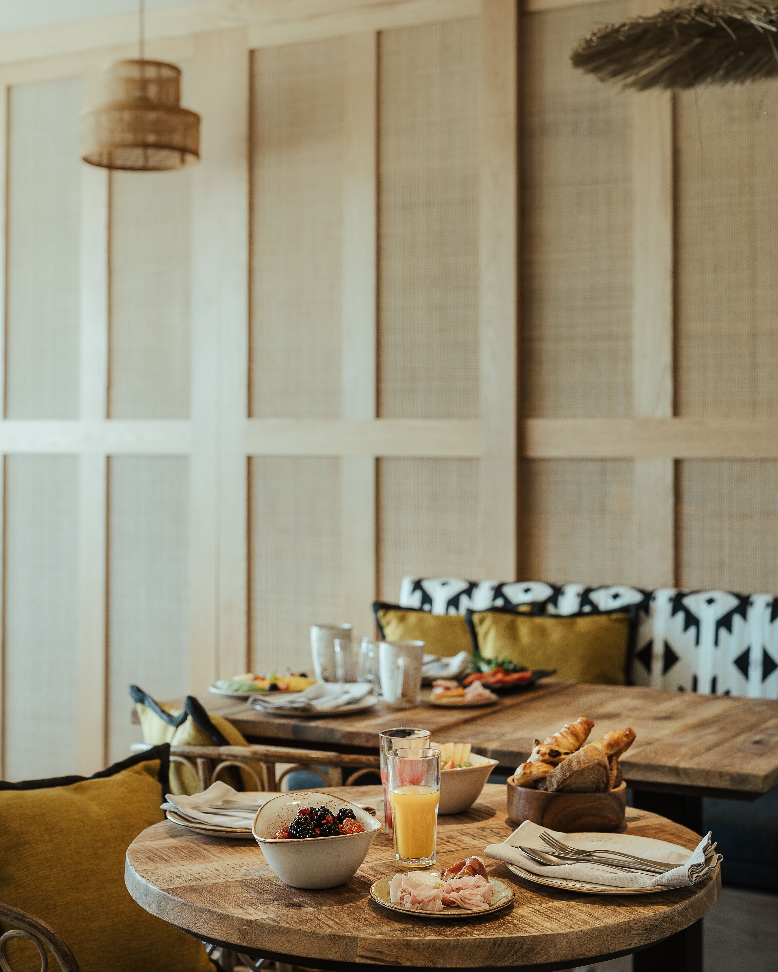 A breakfast setting with a wooden table, plates of food, a bowl of fruit, and a glass of orange juice.