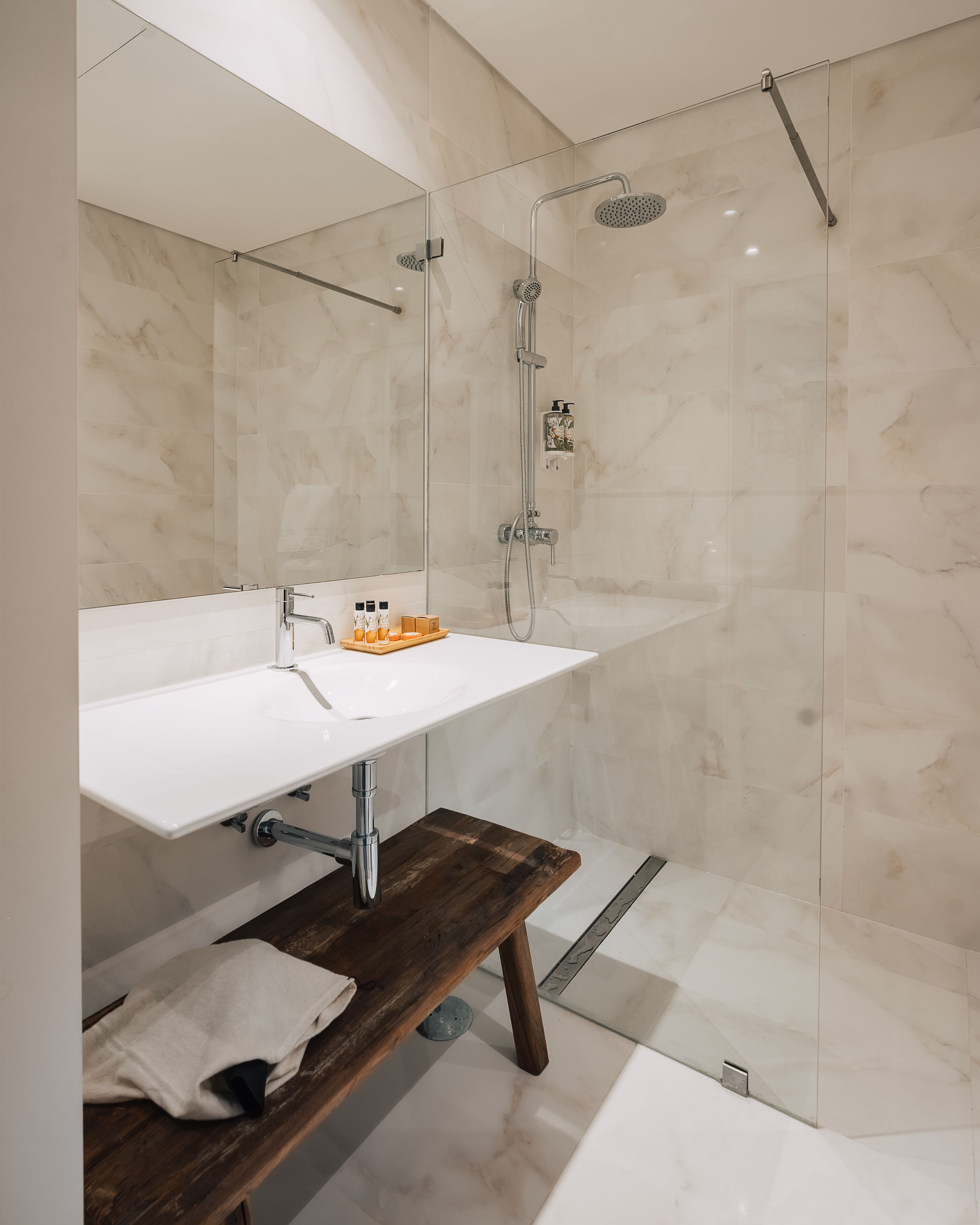 Un bagno moderno con lavabo bianco, panca in legno e cabina doccia in vetro.