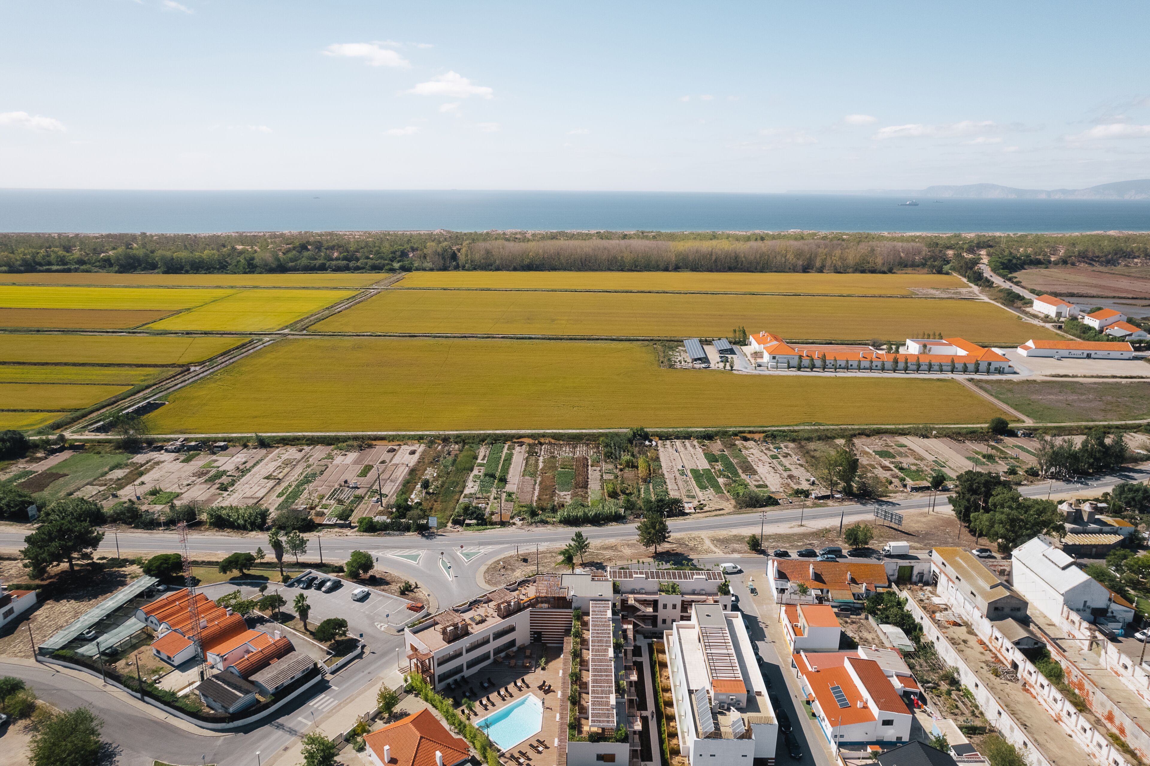 Vista aérea de una zona costera con campos agrícolas, una carretera y edificios con tejados anaranjados.