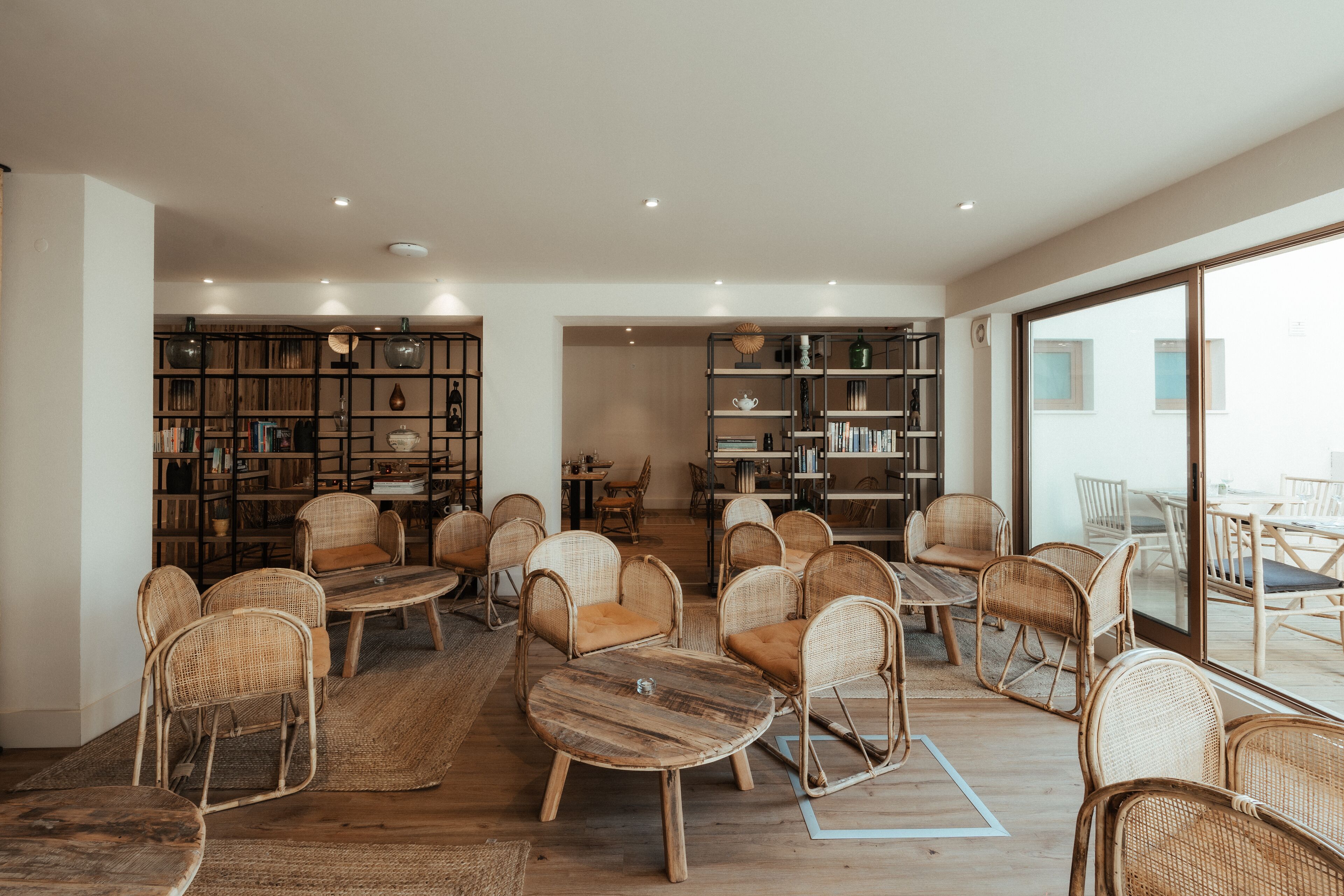 A spacious room with wicker furniture, a large bookshelf, and a view through a glass door.