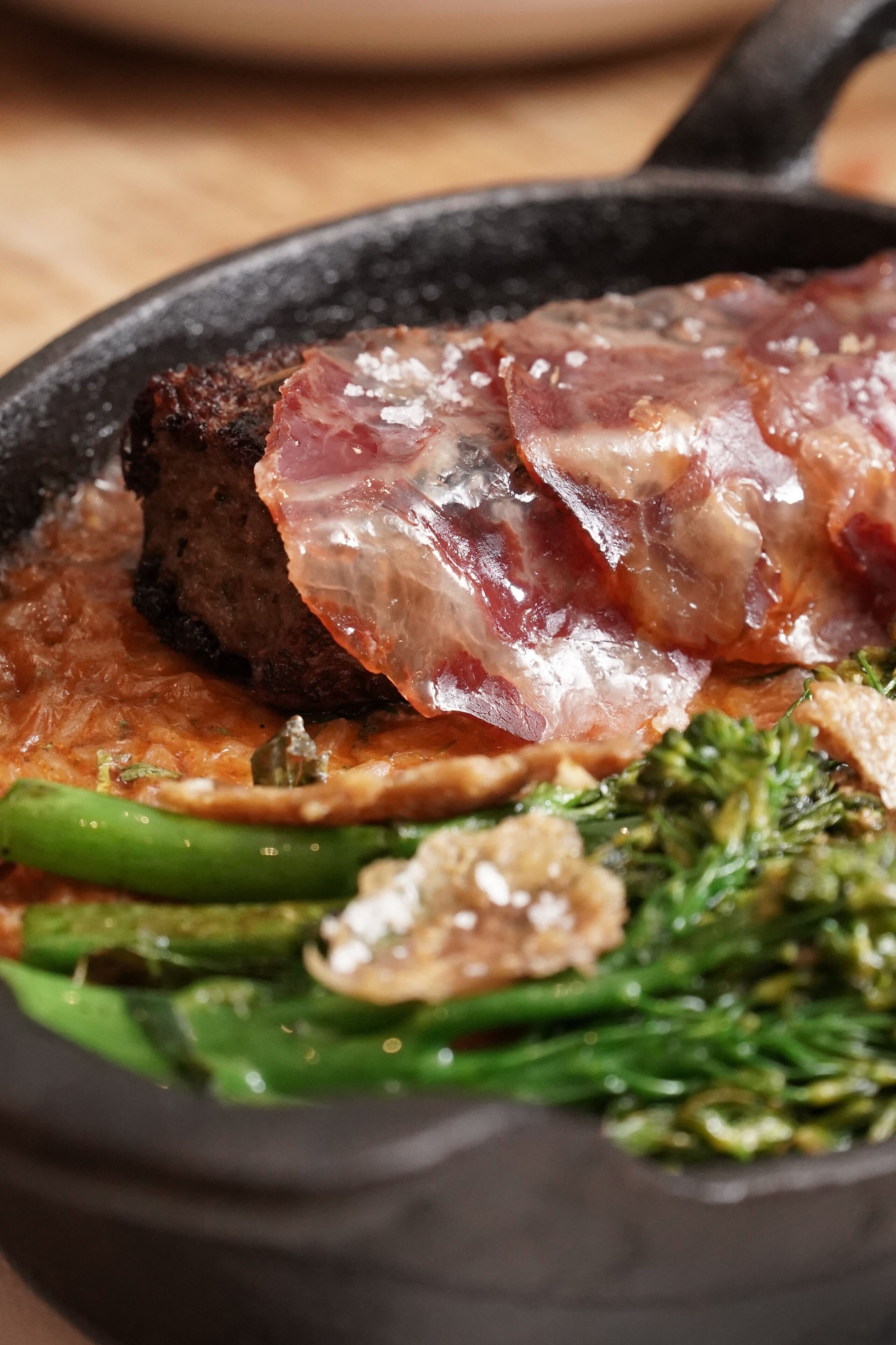 A skillet with a steak, bacon, and vegetables.