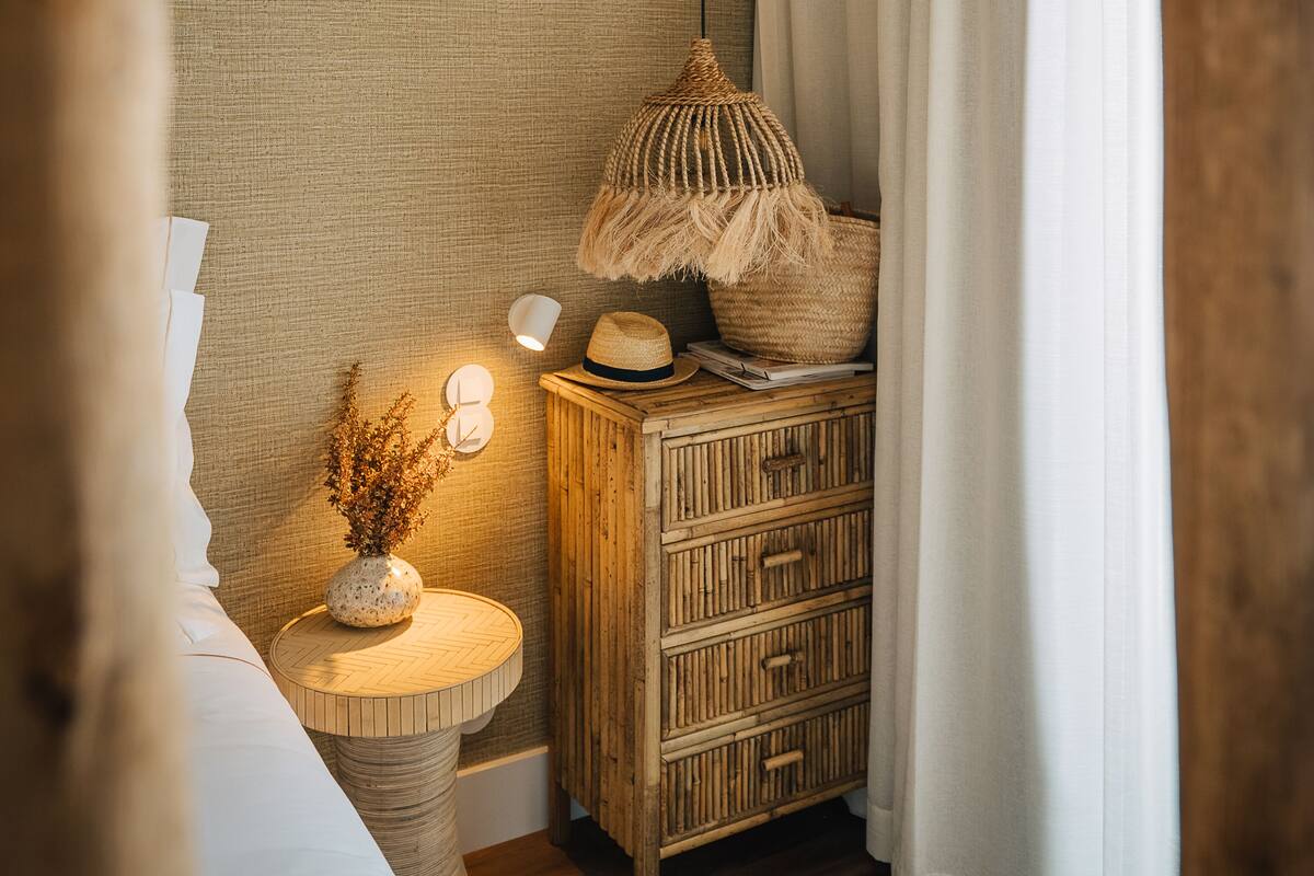 Ein gemütliches Schlafzimmer mit einer Holzkommode, einer gewobenen Lampe und einem kleinen, runden Tisch mit einer Vase.