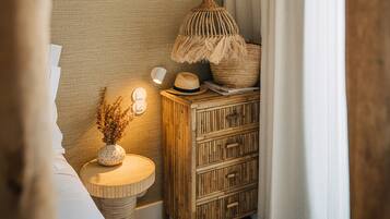A cozy bedroom with a wooden dresser, a woven lamp, and a small round table with a vase.