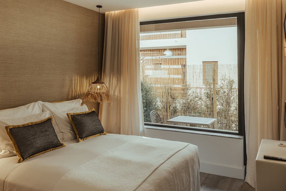 Ein Hotelzimmer mit einem großen Bett, Blick nach draußen und einem kleinen Tisch mit Lampe.