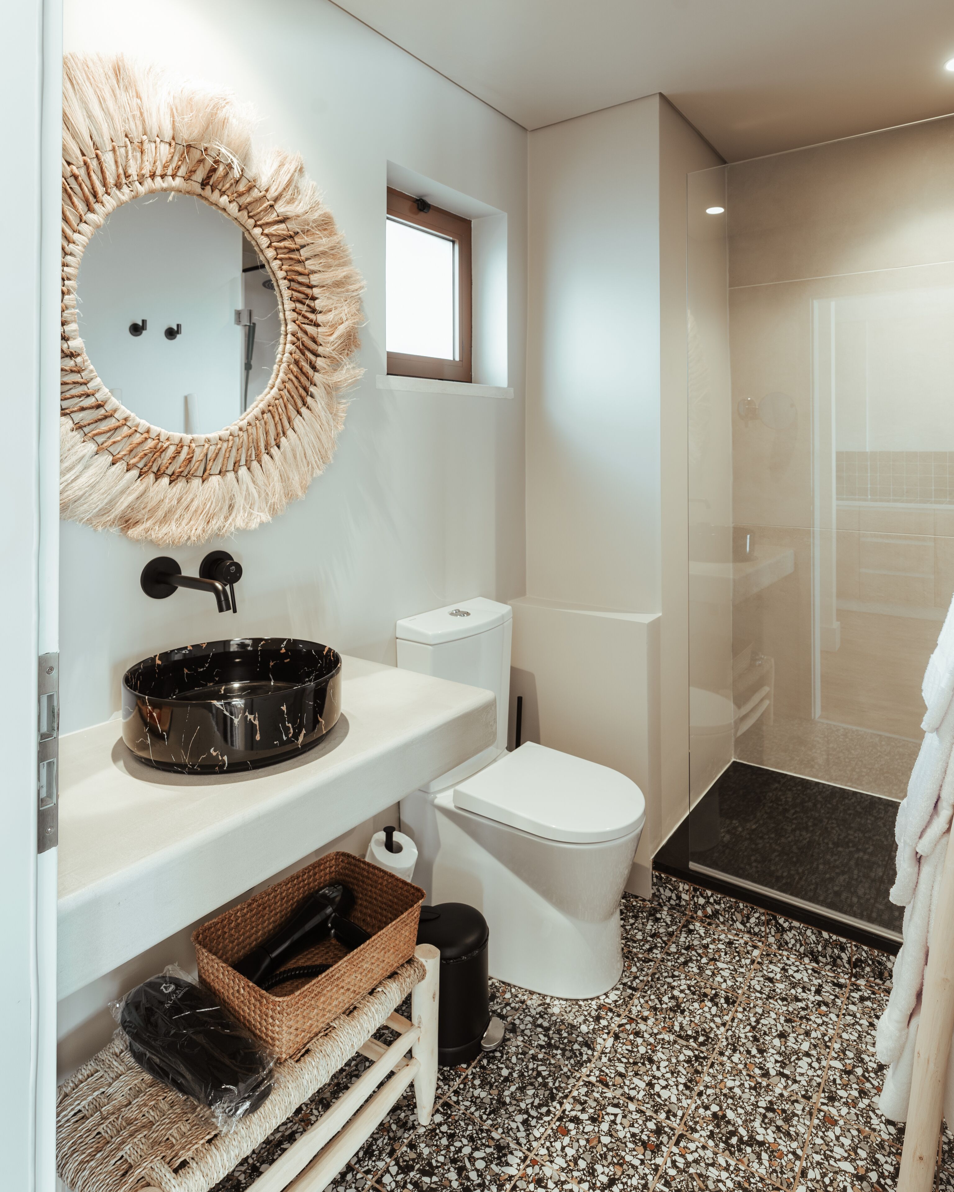 A bathroom with a round mirror, white toilet, and a black sink.