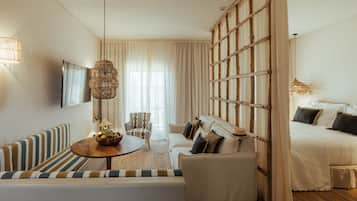 Una habitación de hotel moderna con sofá, una mesa de comedor, una cama y un amplio ventanal con cortinas.