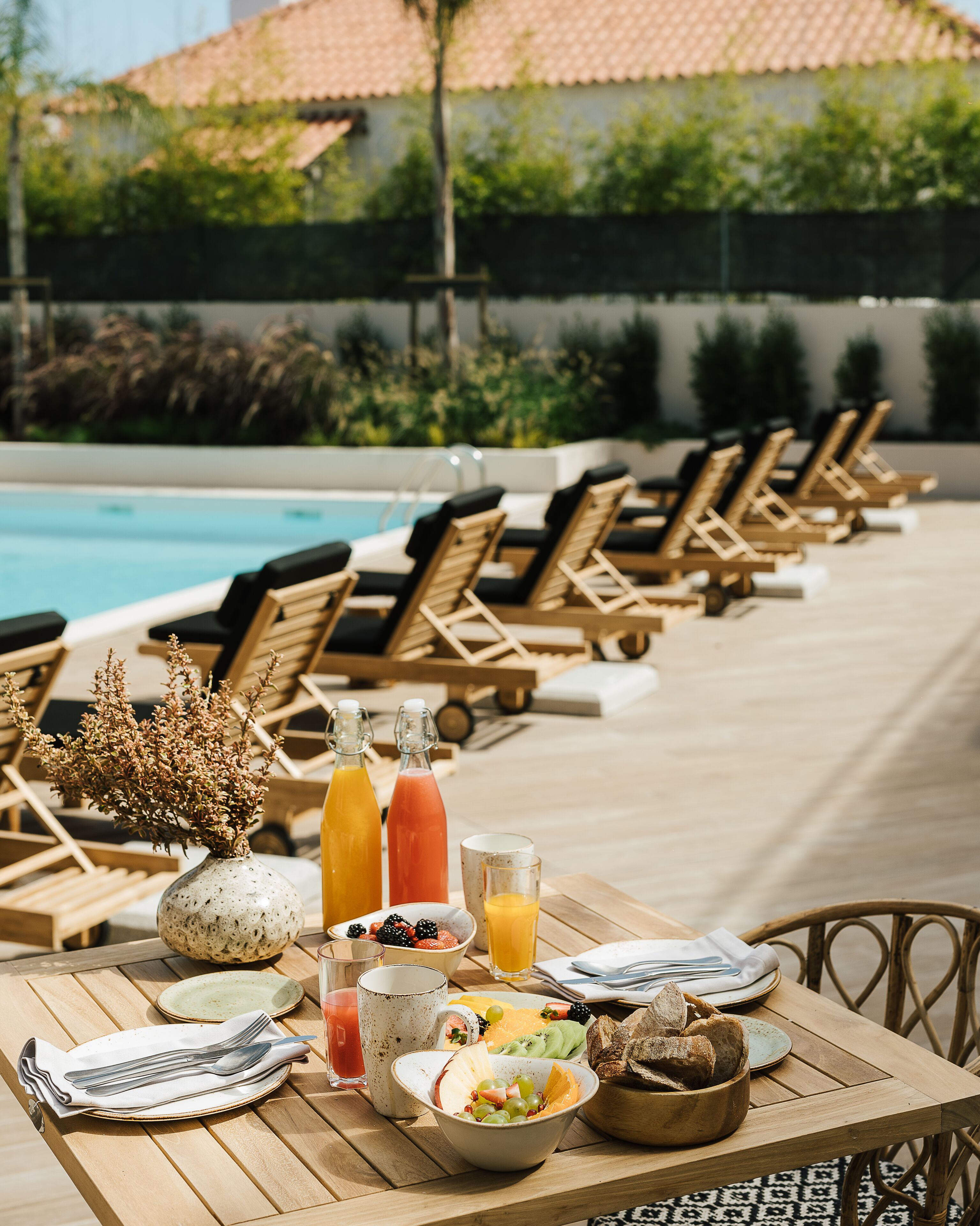 Ein Essbereich am Pool mit Liegestühlen, einem mit Frühstück gedeckten Tisch und einem Pool im Hintergrund.