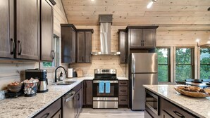 Una cucina moderna con pensili in legno scuro, elettrodomestici in acciaio inossidabile, piani di lavoro in granito e vista sull'esterno grazie a ampie finestre.