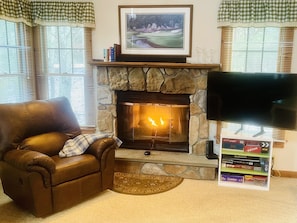 A living room with a stone fireplace, a leather armchair, a flat-screen TV, and a bookshelf with books and decorative items.