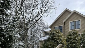 Eine mit Schnee bedeckte Holztreppe führt zu einem beigen Haus mit Fenstern und einem schneebedeckten Dach.