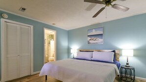 A bedroom with a bed, a ceiling fan, a nightstand with a lamp, and a door leading to a bathroom. - Large private home | Hot tub | Mins to SDC (Branson West)