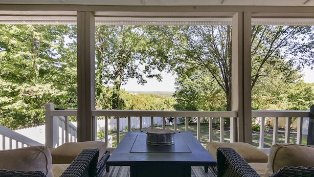 A covered outdoor seating area with wicker furniture and a table, overlooking a scenic landscape. - Large private home | Hot tub | Mins to SDC (Branson West)