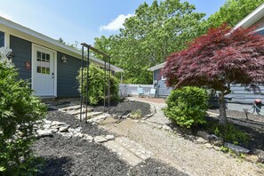 Enjoy a serene escape in a beautifully landscaped garden, surrounded by trees and shrubs, leading to a charming single-story home with a welcoming porch.