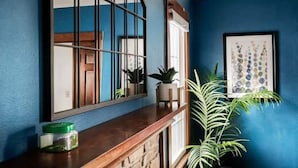 A room with a blue wall, a wooden bench, a large mirror, a framed artwork, and a potted plant.