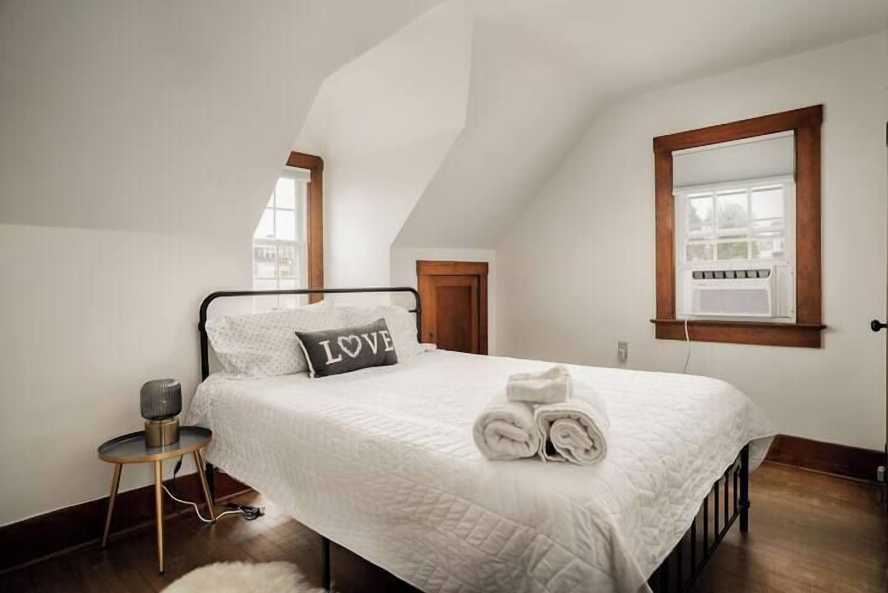 A bedroom with a bed, a bedside table, a lamp, and a window.