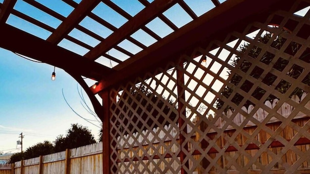 A hot tub under a wooden pergola with a lattice fence in the background.