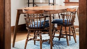 A dining area with a wooden table and chairs, a chandelier, and a shelving unit with plants.