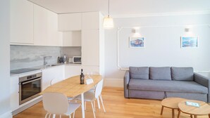 A modern kitchen with white cabinets, a wooden dining table, and a grey sofa. - Feel Porto Downtown Charming Apartment II (Porto)