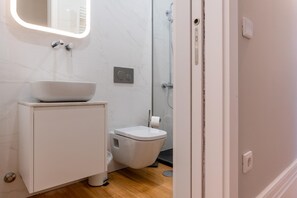 Casa de banho com lavatório branco, sanita e chuveiro.