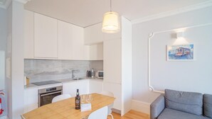 A modern kitchen with white cabinets, a wooden dining table, and a grey sofa. - Feel Porto Downtown Charming Apartment II (Porto)