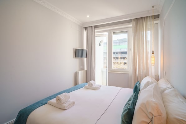 A hotel room with a bed, a TV, and a window with curtains.
