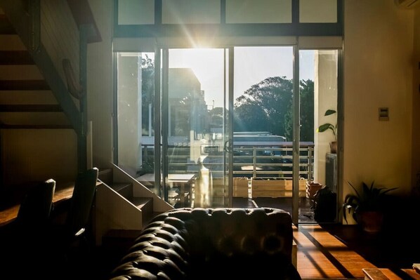 A modern interior with a staircase, a sofa, and a view through large glass doors to the outside.