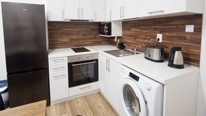 A compact kitchen with white cabinets, a black refrigerator, a microwave, a toaster, and a washing machine. - Aleks Sunrise- Top Center ,Sea Garden (Бургас)