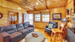 A log cabin interior with a leather sofa, a wooden chair, and a fireplace. - ‘The Deer’ Cabin Peaceful Refuge in East Texas (Ben Wheeler)