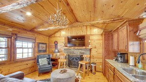 A log cabin interior with a fireplace, wooden furniture, and a kitchen area. - ‘The Deer’ Cabin Peaceful Refuge in East Texas (Ben Wheeler)