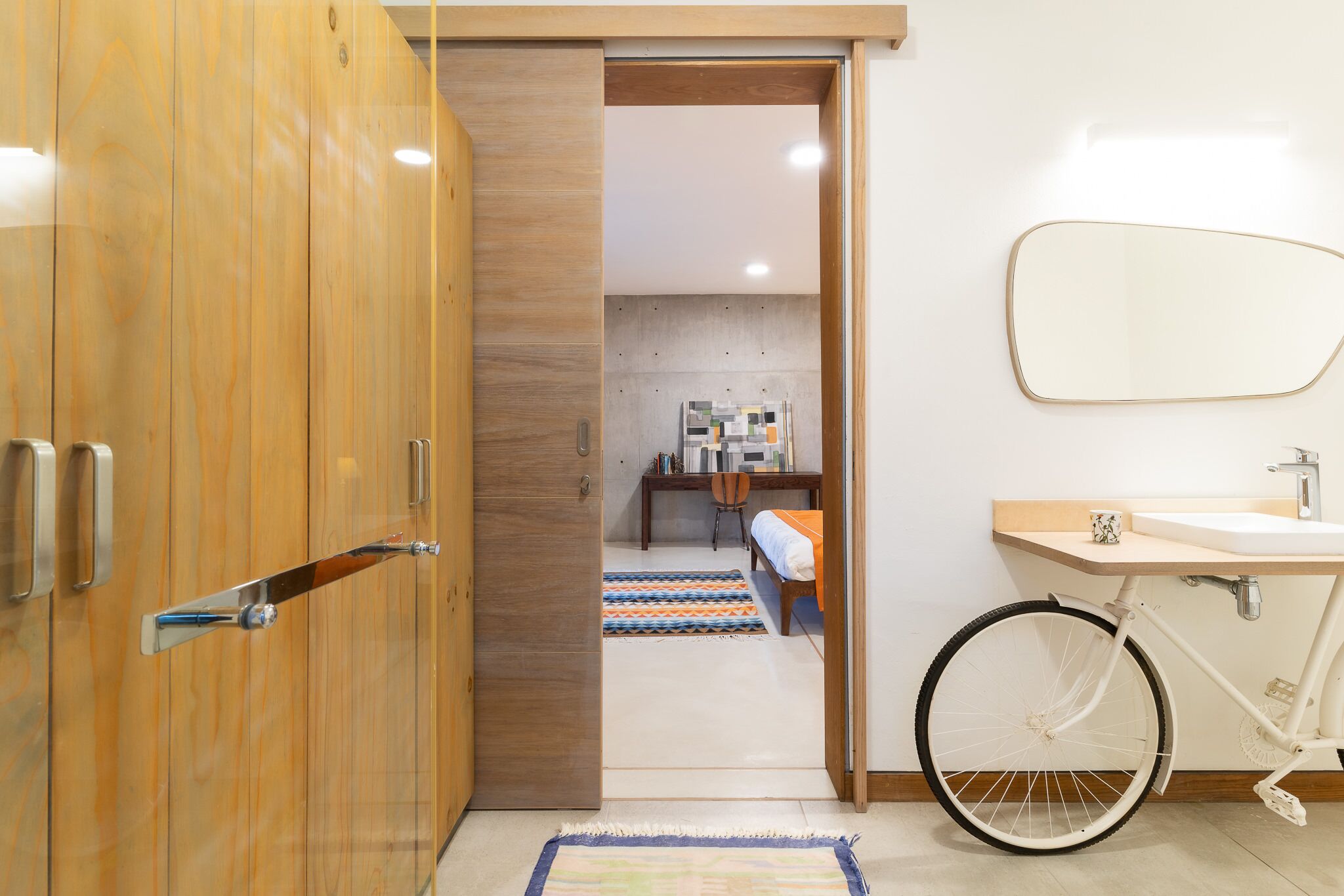 A modern bathroom with a wooden wardrobe, a bicycle, and a small desk with a chair.