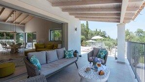 A spacious living area with a sofa, chairs, and a round table. There is a balcony with a railing and outdoor furniture. - Villa Helonaki (Corfu)