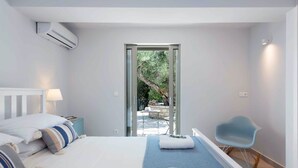 A modern bedroom with a bed, bedside table, lamp, and a view of an outdoor patio. - Villa Helonaki (Corfu)