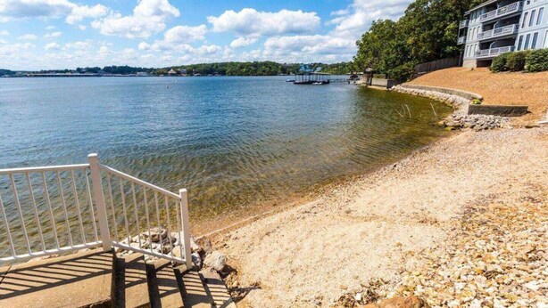 A waterfront property with a clear view of the lake, a wooden deck, and a building with multiple balconies. - Turtle Haven - Relax & Enjoy the Incredible Views! (Osage Beach)