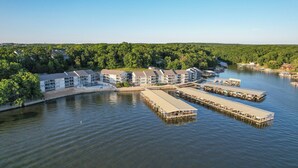 A waterfront hotel with multiple docked boats, a marina, and a forested backdrop. - Turtle Haven - Relax & Enjoy the Incredible Views! (Osage Beach)