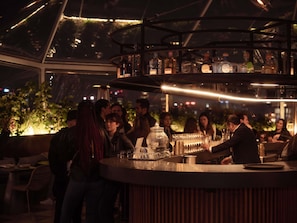 A bar area with a circular counter, shelves with bottles, and a view of the outdoors. - Mondrian Mexico City Condesa  (Mexico City)