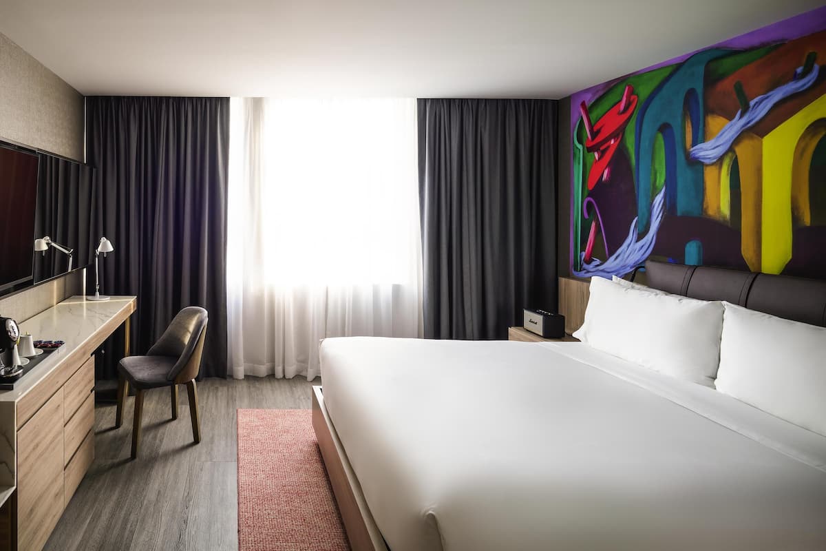 Een hotelkamer met een bed, een bureau, een stoel, een televisie en een schilderij aan de muur.