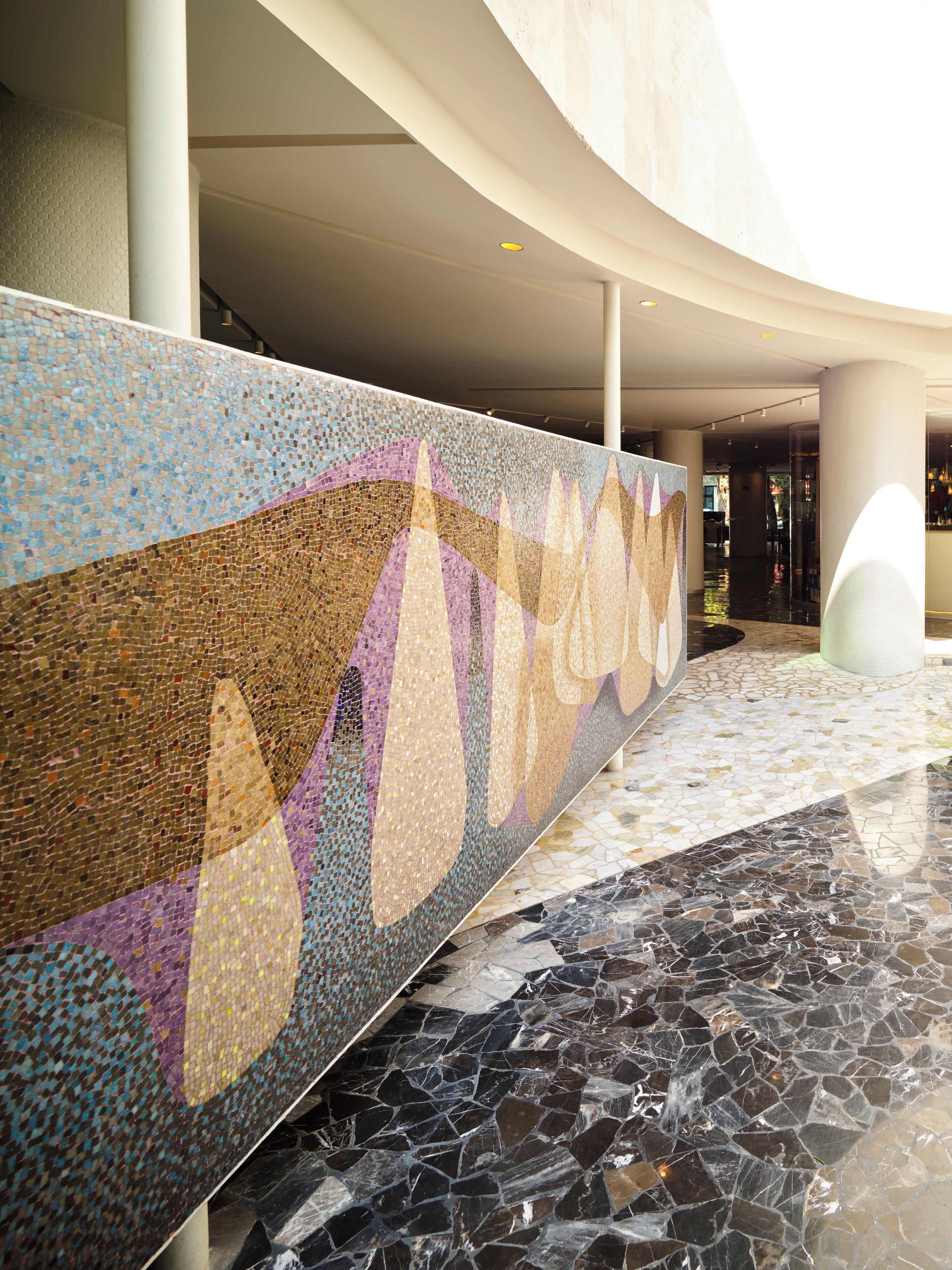 Eine Wand mit Mosaikdekor, ein Marmorboden und eine gewölbte Deckenstruktur.