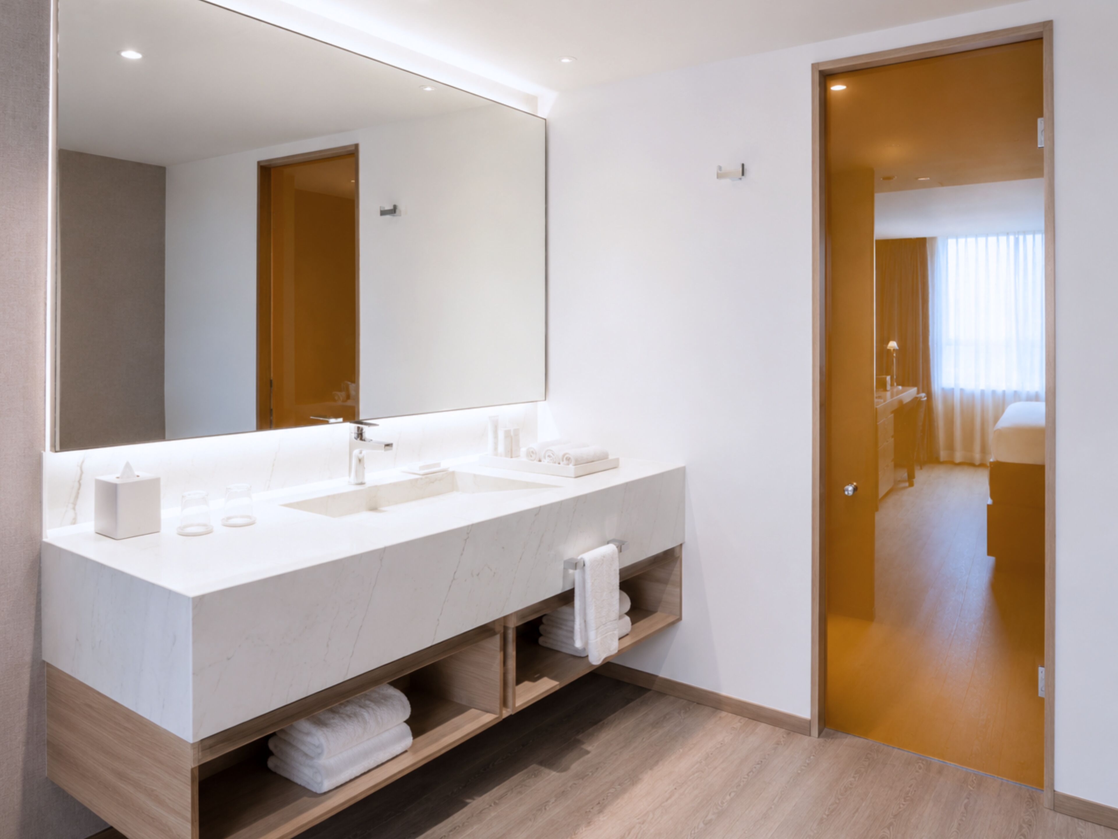 A modern bathroom with a large mirror, two sinks, and a wooden vanity.